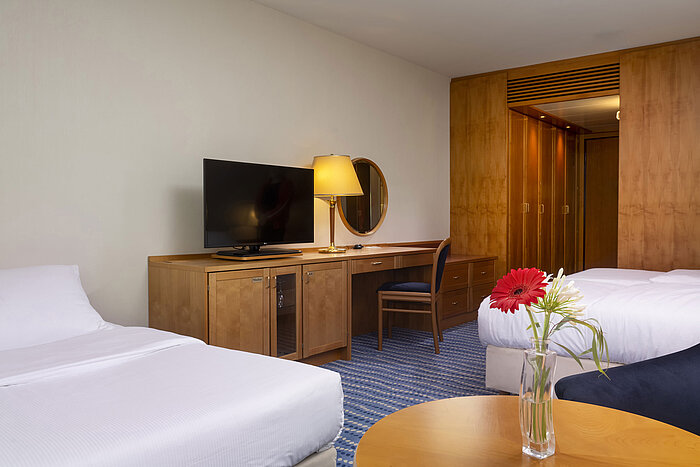 Classic Familienzimmer Classic Familienzimmer mit zwei Betten, Schreibtisch, Flachbildfernseher und Vase mit frischen Blumen auf dem Tisch