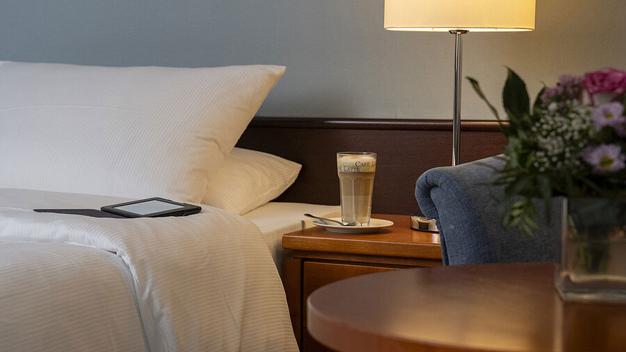 Classic Zimmer Detailaufnahme eines gemütlichen Classic-Zimmers mit Bett, Nachttisch, Latte Macchiato und moderner Beleuchtung.