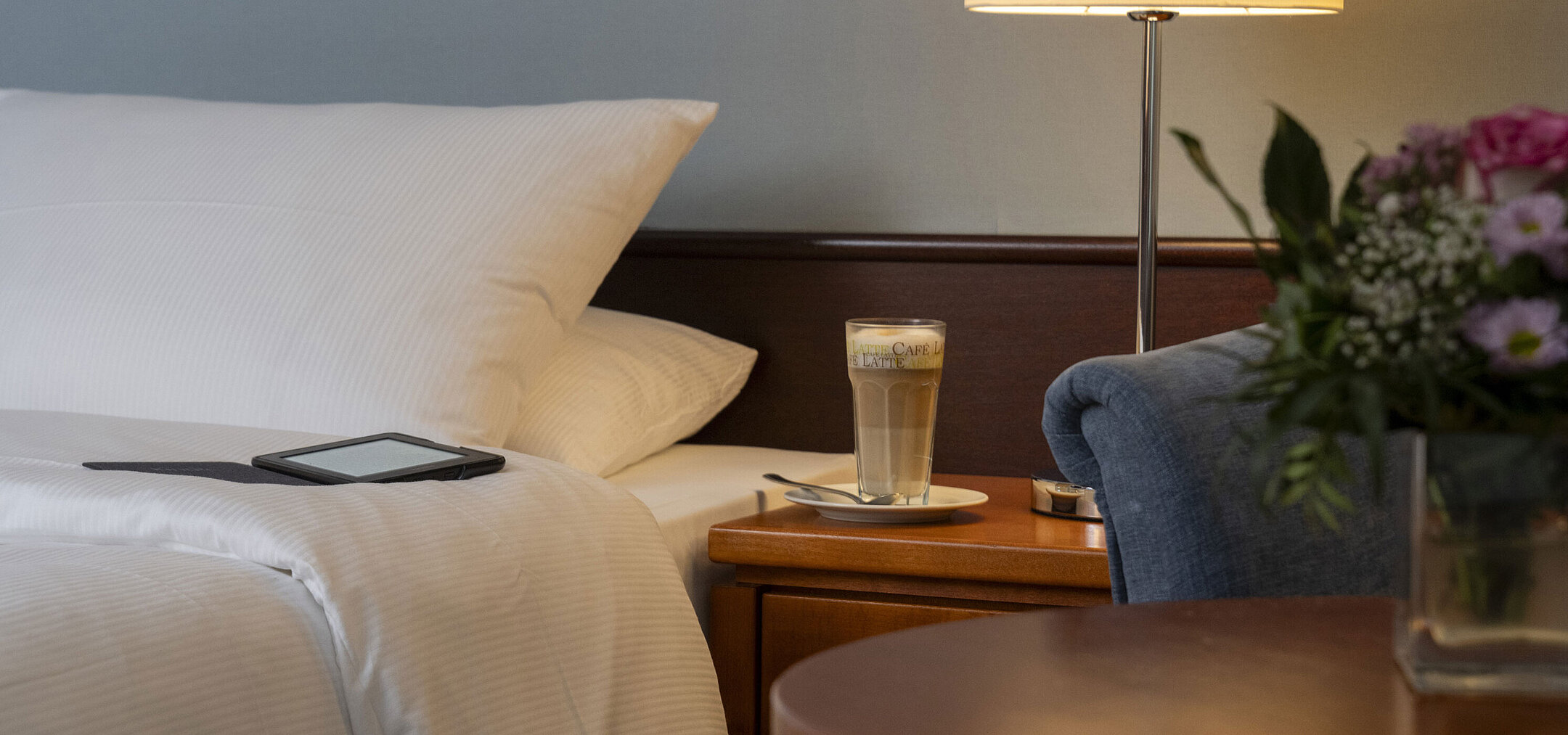 Classic Zimmer Detailaufnahme eines gemütlichen Classic-Zimmers mit Bett, Nachttisch, Latte Macchiato und moderner Beleuchtung.
