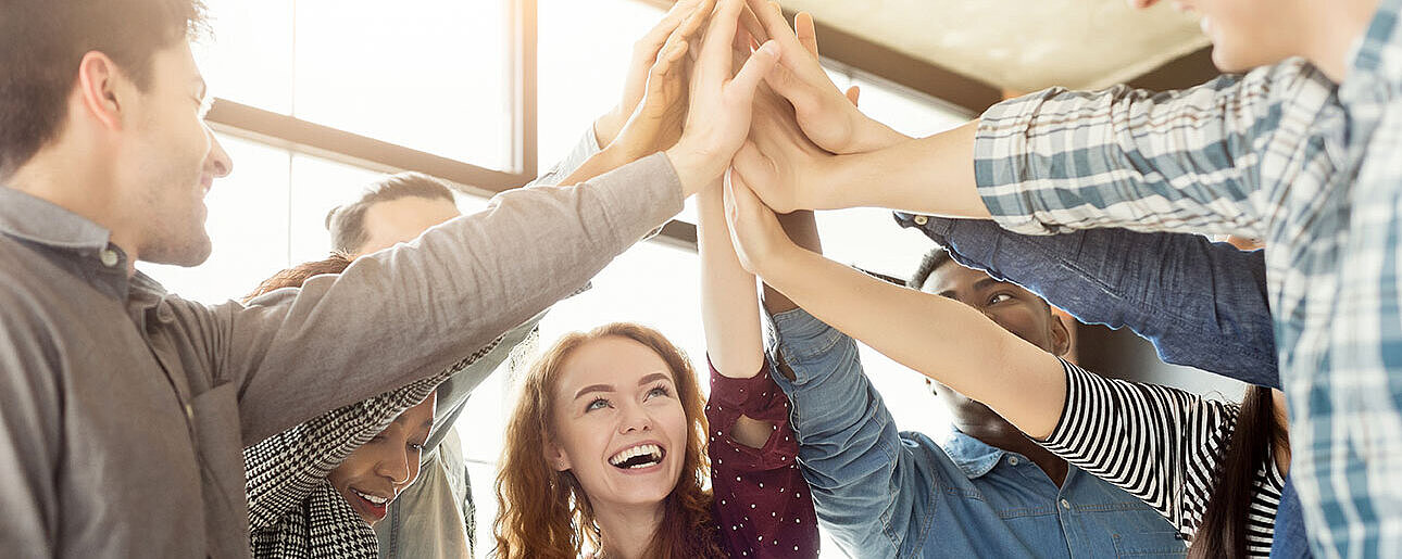 © Prostock-studio - AdobeStock.com Gruppe von jungen Menschen gibt sich ein High-Five und feiert gemeinsam einen Erfolg.