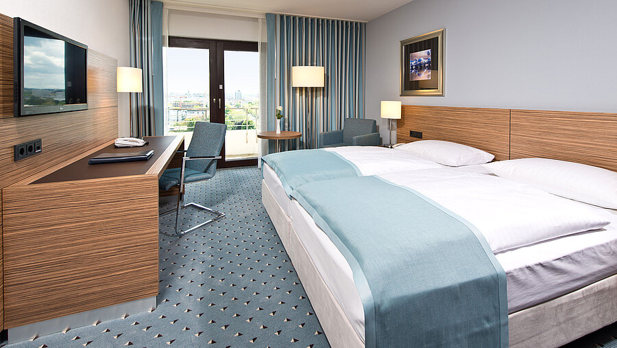 Comfort Zimmer Comfort Zimmer im Maritim Hotel Darmstadt mit modernem Design, Schreibtisch, Sitzbereich und Blick auf große Fenster.