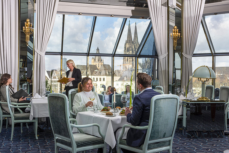 Restaurant "Bellevue" Restaurant "Bellevue" im Maritim Hotel Köln mit Gästen, die speisen, und Blick auf den Kölner Dom durch große Fenster.