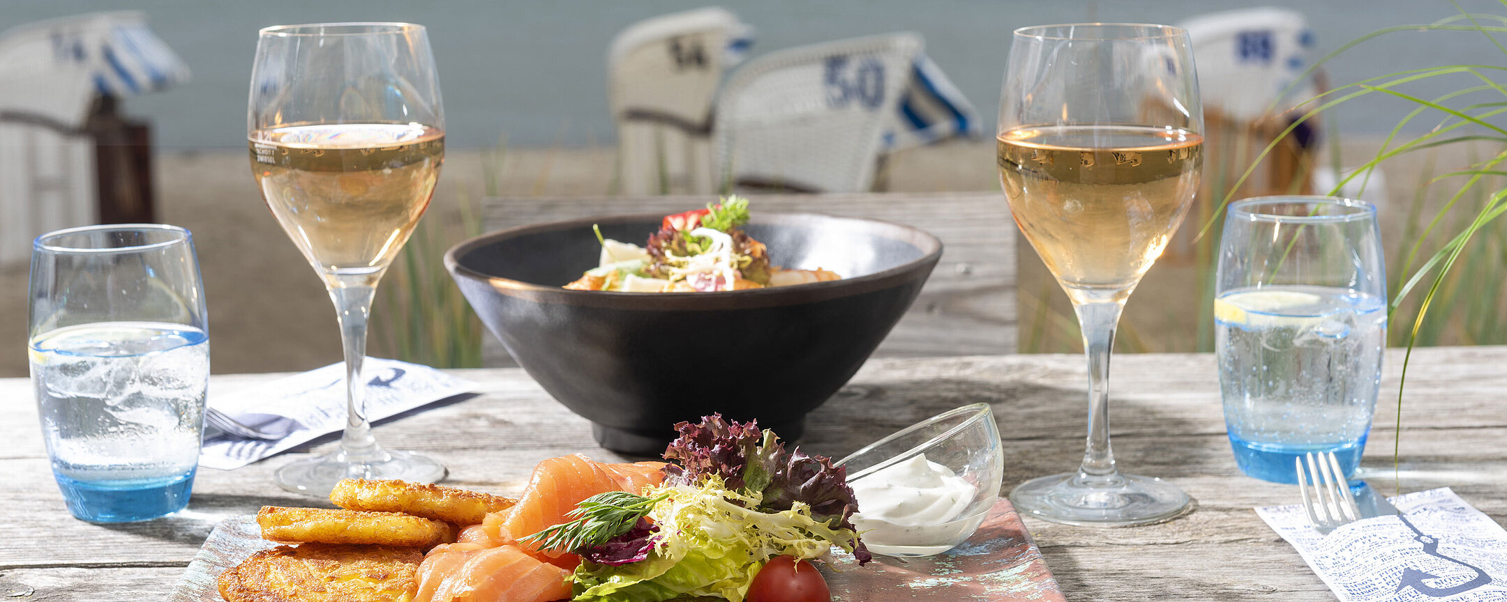 Beach Lounge Gedeckter Tisch mit Fischgericht und Wein auf einer Terrasse mit Blick auf das Meer.
