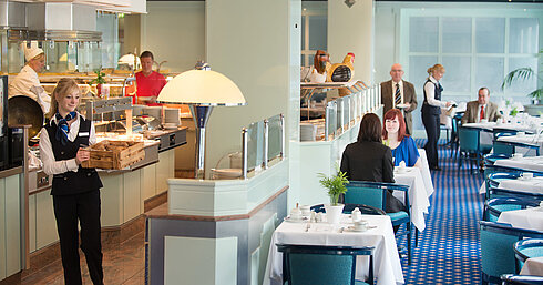 Restaurant "Sinfonie" Eine Kellnerin bringt frische Brötchen zum Frühstücksbereich im Maritim Hotel Magdeburg, während Gäste am Tisch sitzen.