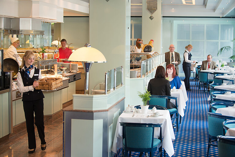 Restaurant "Sinfonie" Eine Kellnerin bringt frische Brötchen zum Frühstücksbereich im Maritim Hotel Magdeburg, während Gäste am Tisch sitzen.