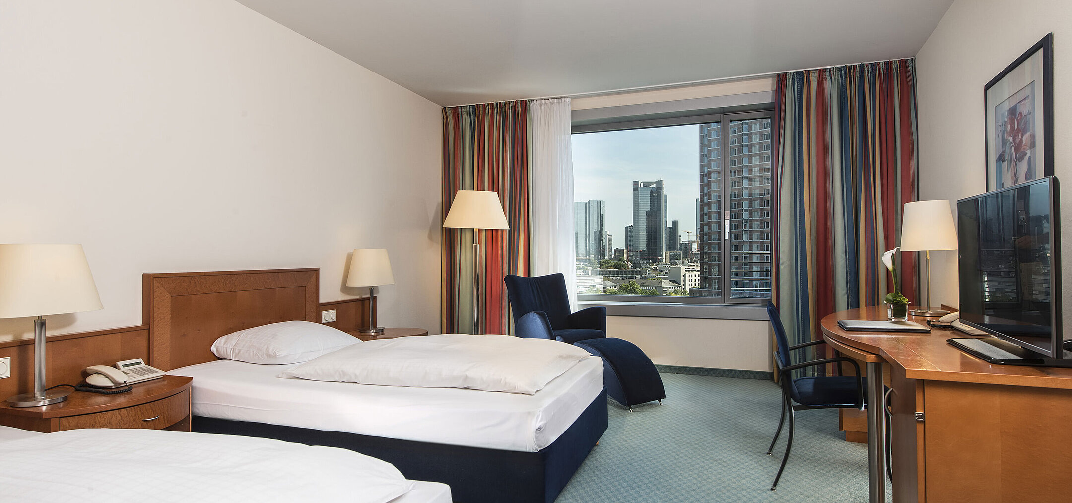 Comfort Zimmer Comfort Zimmer im Maritim Hotel Frankfurt mit zwei Einzelbetten, Schreibtisch, Sitzbereich und Blick auf die Skyline.