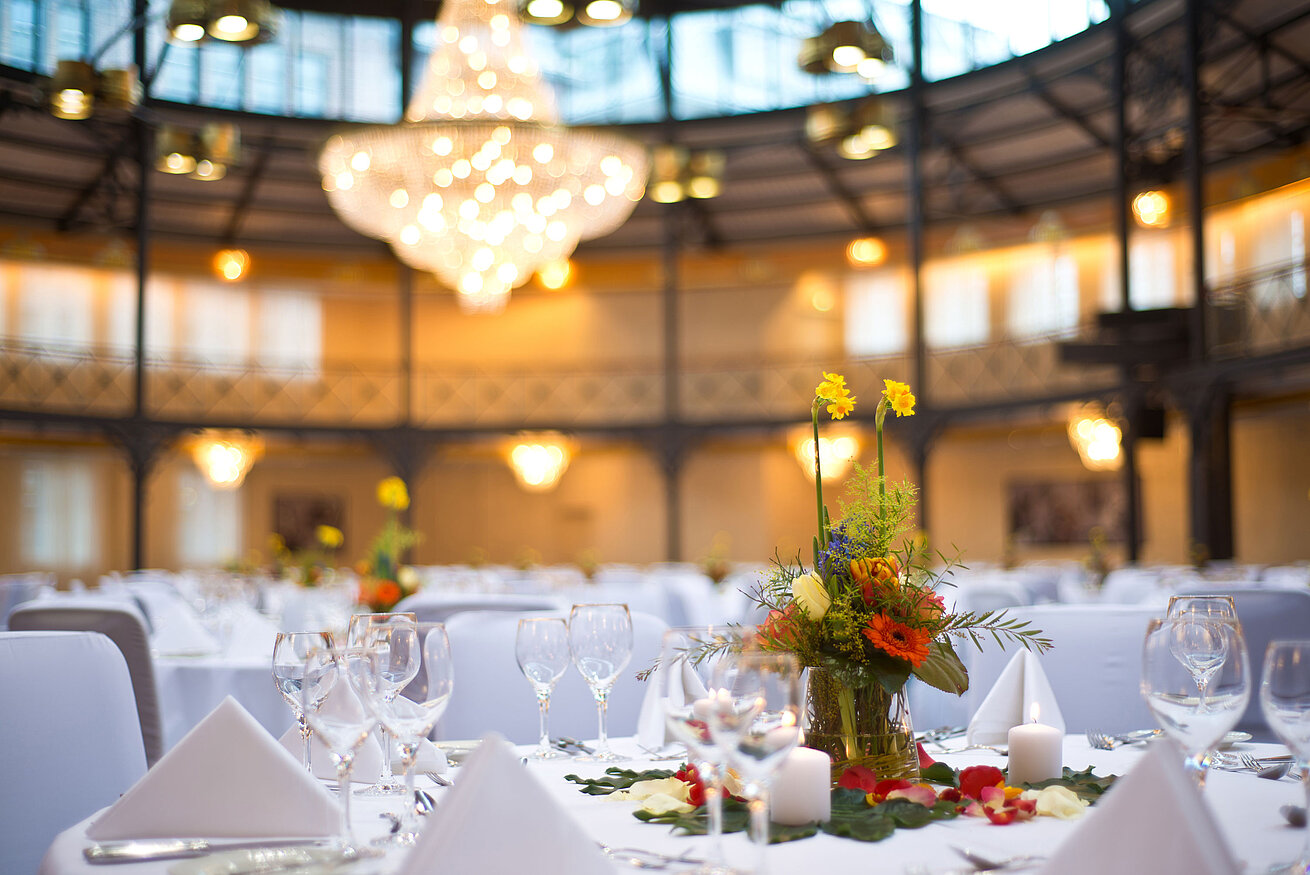 Detailansicht Tagungsraum Nahaufnahme einer Tischdekoration mit Blumen und Kerzen, im Hintergrund ein großer Kronleuchter