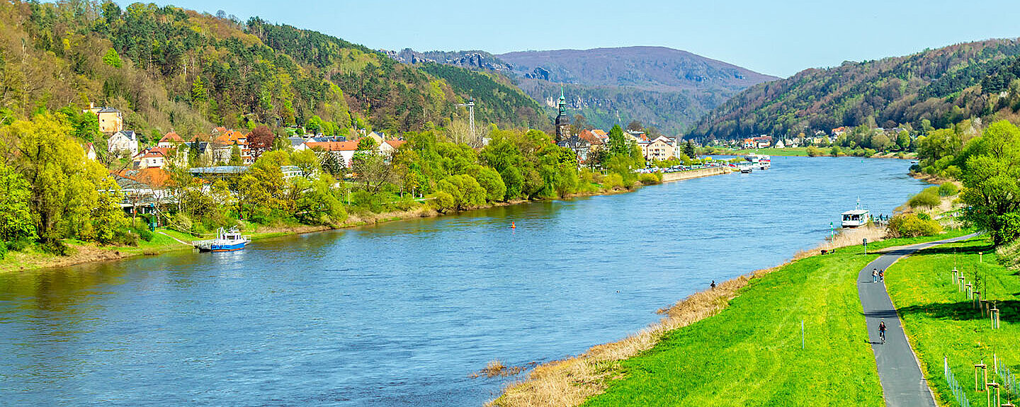 © Oliver_Hlavaty - AdobeStock.com Elbe bei Dresden mit grünen Ufern, sanften Hügeln und weiter Landschaft unter blauem Himmel.
