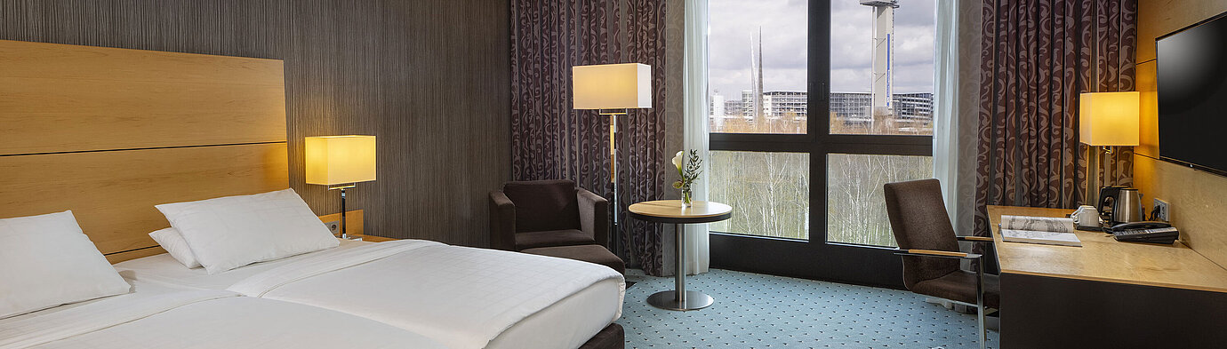 Classic Zimmer Classic Zimmer im Maritim Hotel Düsseldorf mit Doppelbett, Schreibtisch und Panoramafenster mit Blick auf die Umgebung.