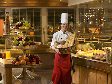 Restaurant "Rôtisserie" Bäcker mit Brotkorb am Frühstücksbuffet des Maritim Hotel Stuttgart, umgeben von frischem Obst