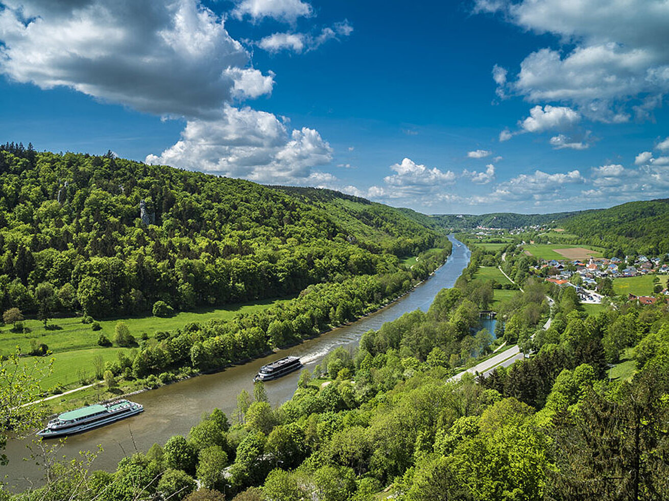© Andy Ilmberger - AdobeStock.com Schiffe auf der Altmühl im Altmühltal, umgeben von grünen Hügeln und blauem Himmel