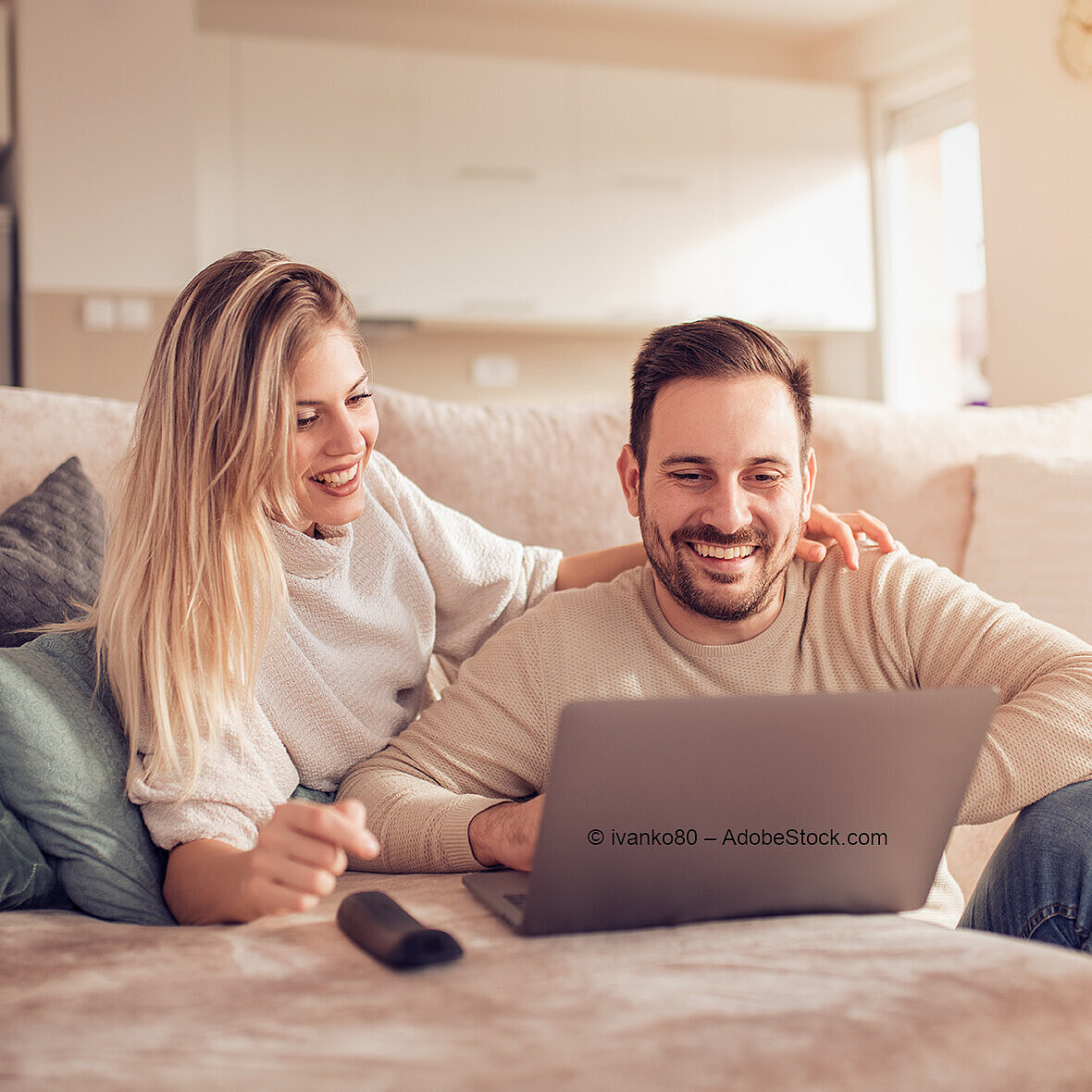 © ivanko80 - AdobeStock.com Paar sitzt entspannt auf dem Sofa und schaut gemeinsam auf Laptop