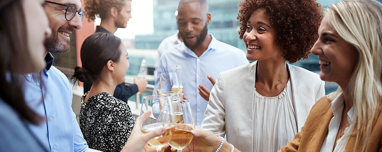 © Monkey Business - AdobeStock.com Kolleg:innen stoßen bei einem Business-Event mit Getränken an und genießen den gemeinsamen Austausch.