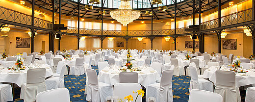 Alte Stuttgarter Reithalle Bankett runde Tische Frontalansicht des prachtvollen Bankettsaals mit weiß gedeckten Tischen und floraler Dekoration