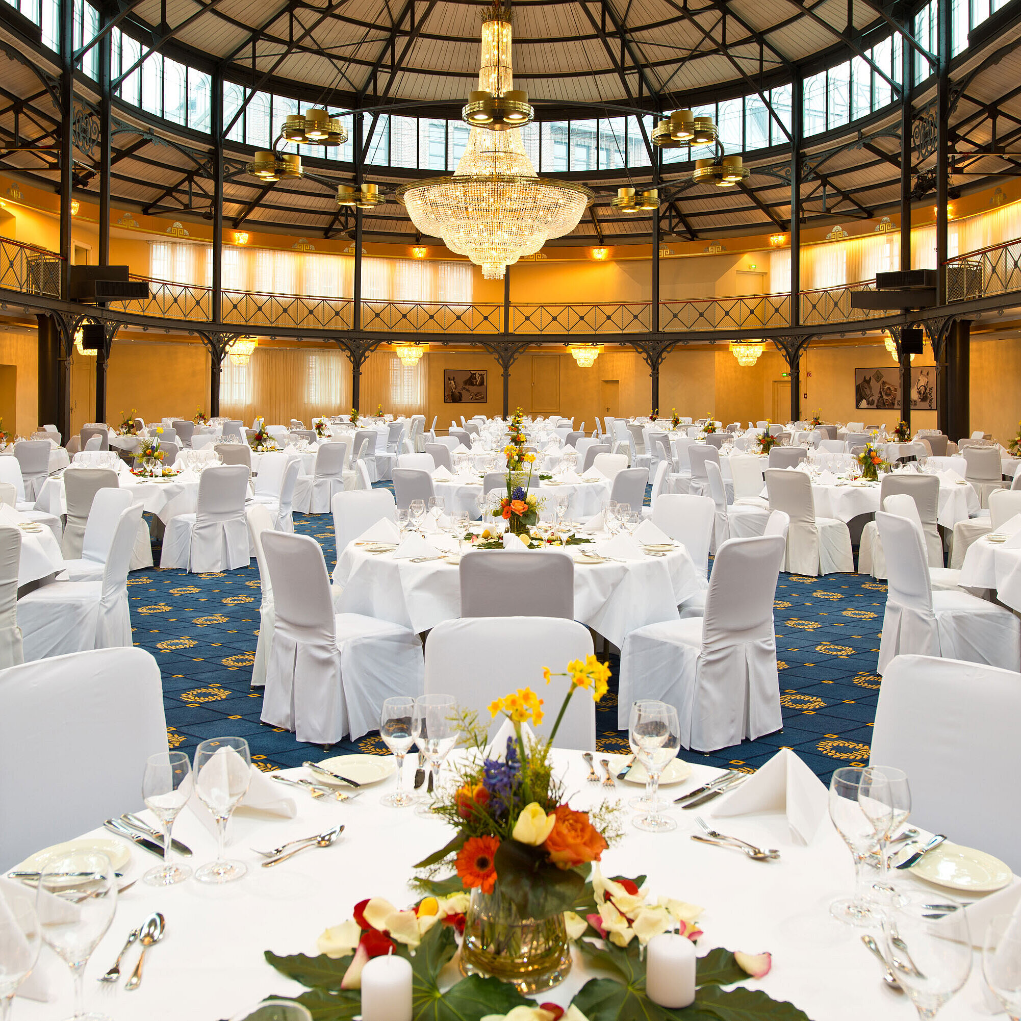 Alte Stuttgarter Reithalle Bankett runde Tische Frontalansicht des prachtvollen Bankettsaals mit weiß gedeckten Tischen und floraler Dekoration