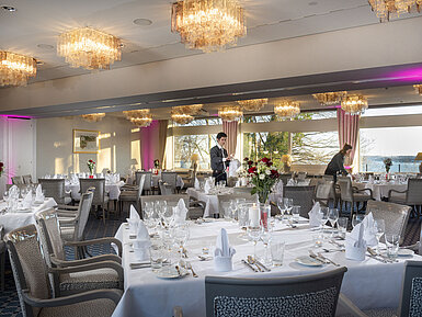 Salon Kopenhagen und Helsinki Salons Kopenhagen und Helsinki im Maritim Hotel Kiel, gedeckte Tische, Kronleuchter und Meerblick, Personal richtet den Raum.