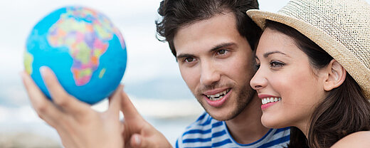 © contrastwerkstatt - AdobeStock.com Junges Paar schaut auf kleinen Globus und plant die nächste Reise