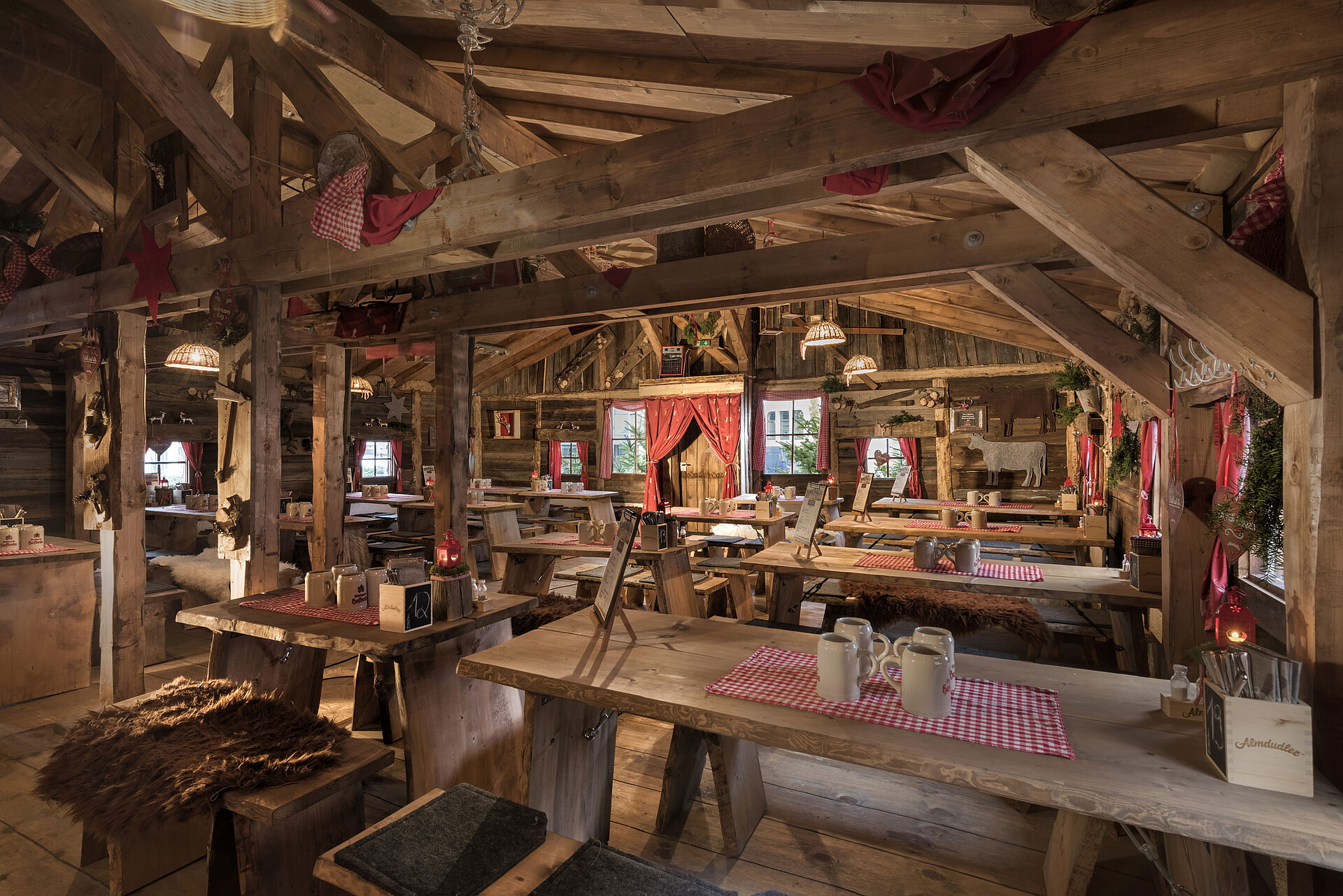 Almhütte Warmer Innenbereich mit Holztischen, roten Vorhängen und uriger Deko in der Maritim Alm Stuttgart
