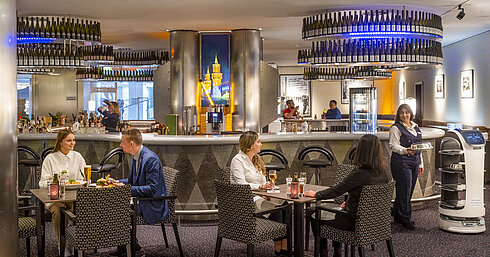 Restaurant & Bar Checkpoint Gäste speisen in der Bar des Maritim proArte Hotel Berlin, umgeben von modernen Einrichtungen und einem Serviceroboter.