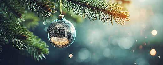 © Synthetica - AdobeStock.com Christbaumkugel hängt an Tannenzweig mit weihnachtlicher Beleuchtung
