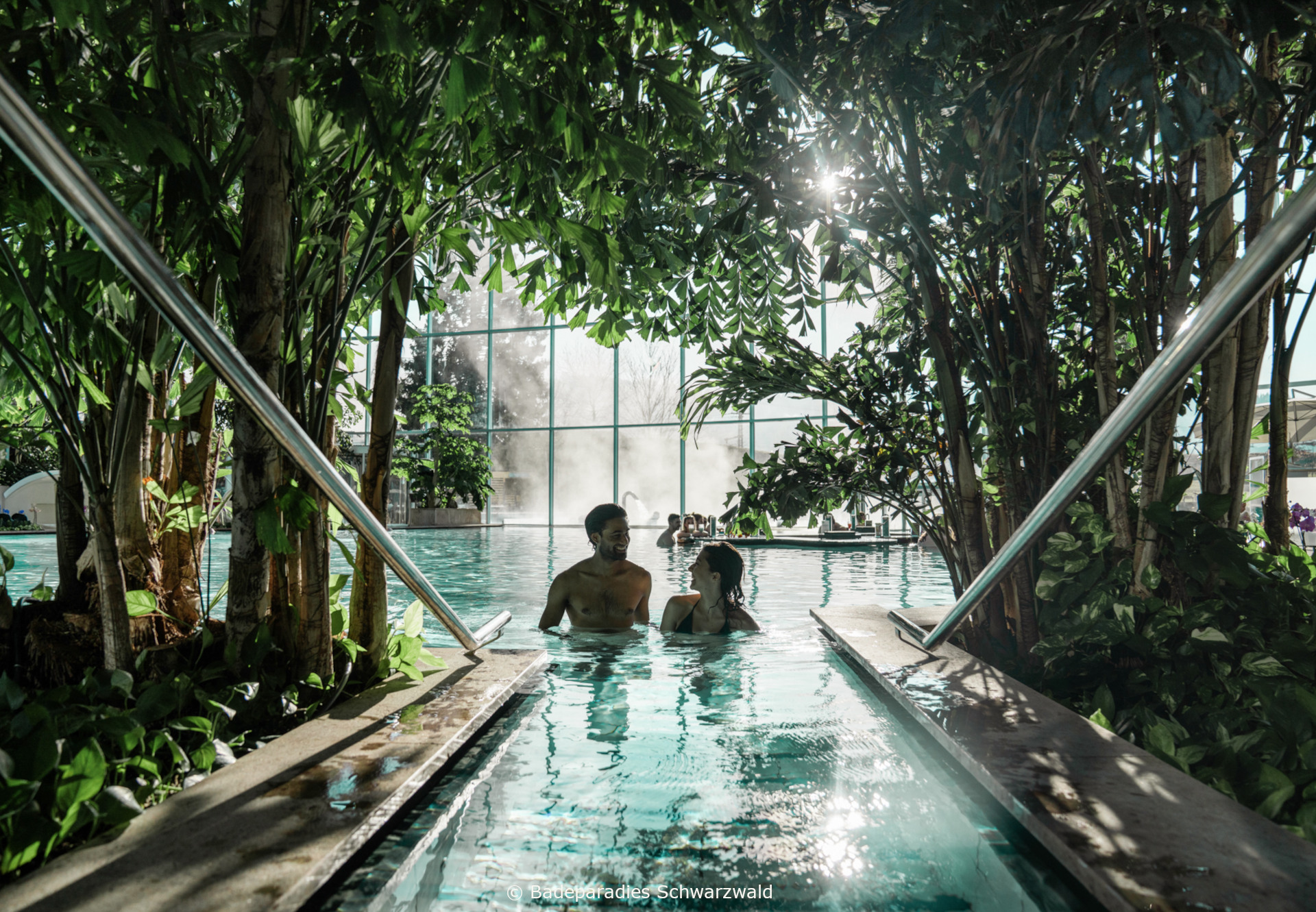Palmenoase © Badeparadies Schwarzwald Zwei Personen entspannen im Indoor-Pool mit tropischer Begrünung und Tageslicht