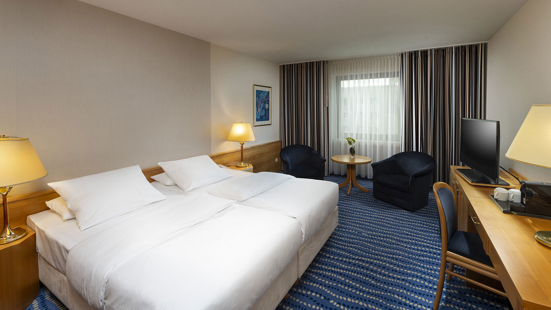 Superior Zimmer Großes Bett mit Nachttischen und Lampen, daneben Sitzbereich und Schreibtisch.