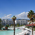 Panorama des Maritim Resort Calabria mit Pool, Palmen, weißen Gebäuden und Bergkulisse im Hintergrund bei klarem Himmel.