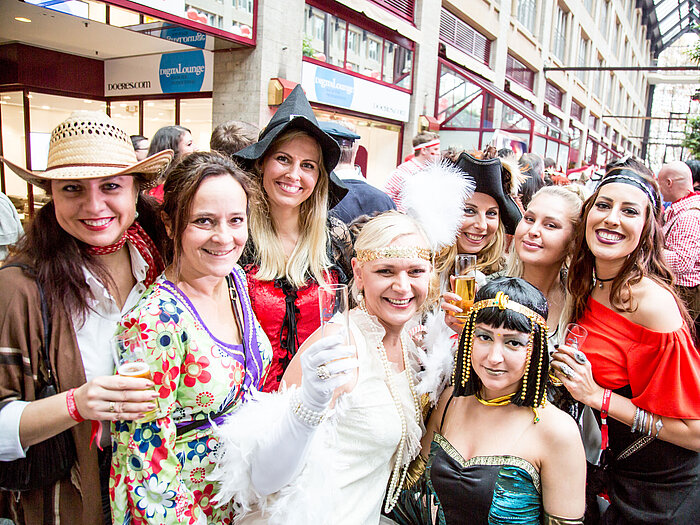 Frauen in bunten Kostümen feiern auf einem Karneval und halten Sektgläser in die Kamera.