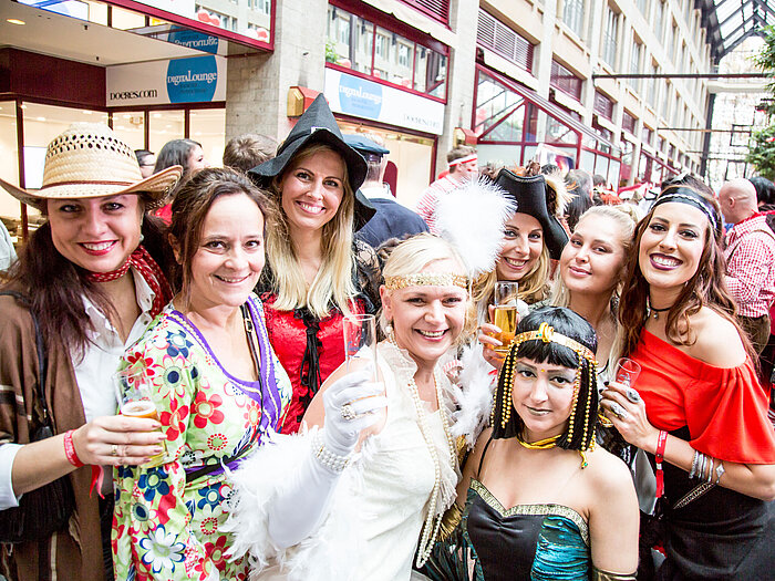 Frauen in bunten Kostümen feiern auf einem Karneval und halten Sektgläser in die Kamera.