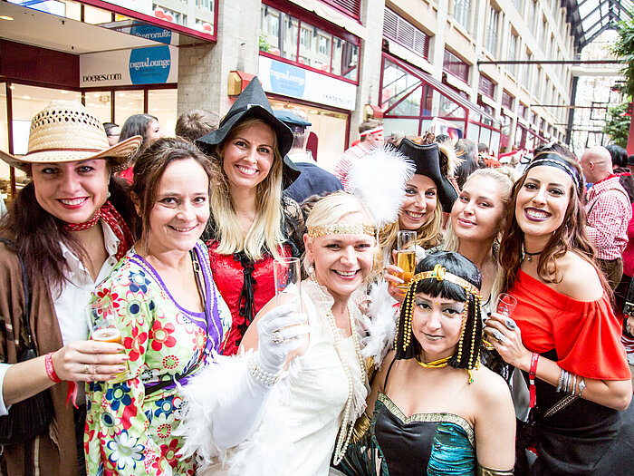 Frauen in bunten Kostümen feiern auf einem Karneval und halten Sektgläser in die Kamera.