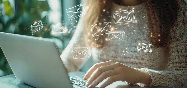 © Tanuha - AdobeStock.com Frau arbeitet am Laptop mit digitalen Symbolen für E-Mail-Kommunikation im modernen Büro