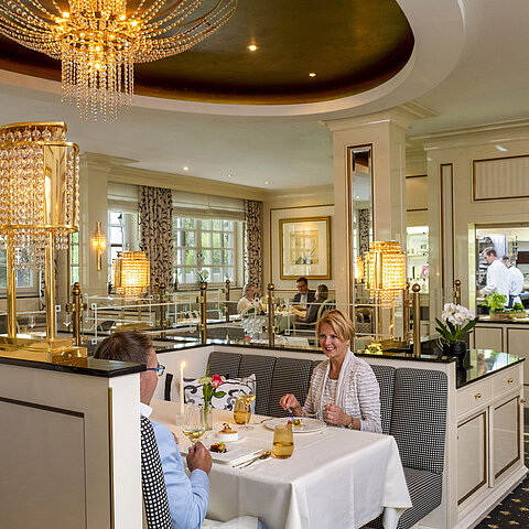 Paar genießt ein feines Dinner im luxuriösen Restaurant Orangerie des Maritim Timmendorfer Strand mit Blick in die Küche.