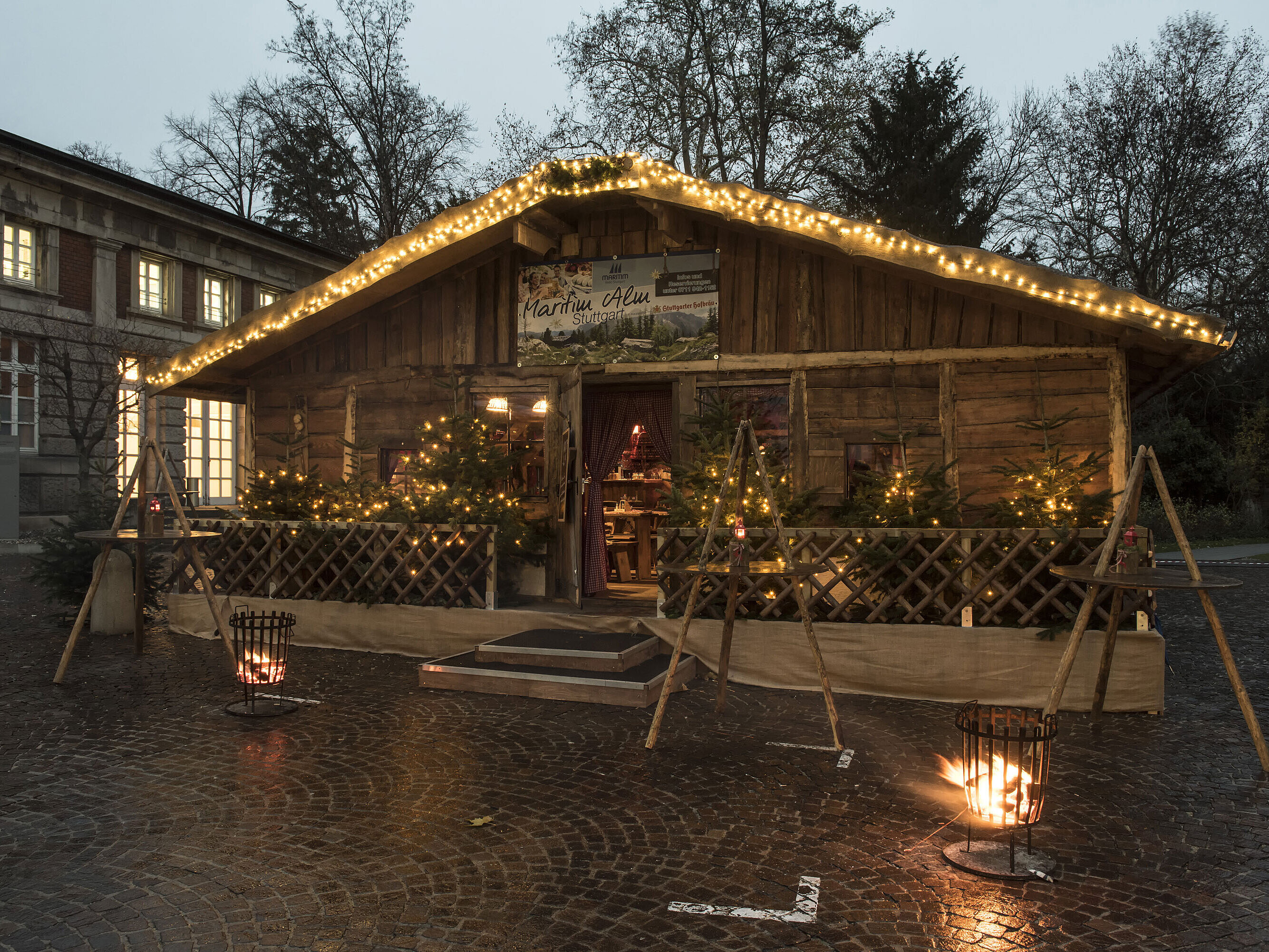 Maritim Alm Stuttgart Maritim Alm Stuttgart bei Dämmerung mit Weihnachtsbeleuchtung, Tannen und Feuerkörben vor dem Maritim Hotel