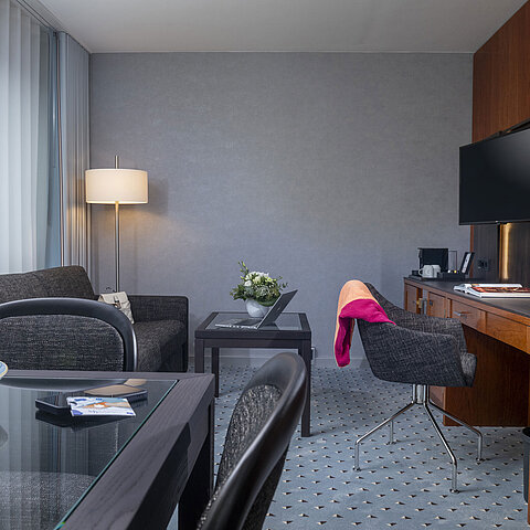 Elegantes Suite-Wohnzimmer im Maritim Bremen mit gemütlicher Sitzecke, Schreibtisch, TV und frischen Blumen als Dekoration.