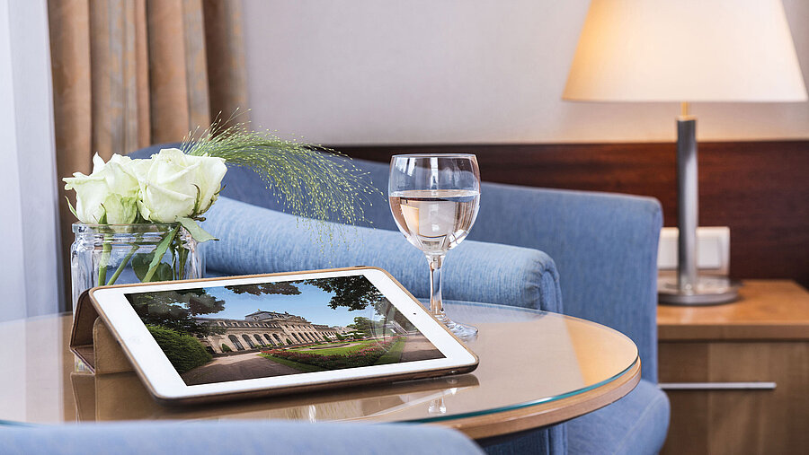Zimmerdetail Gemütlicher Sitzbereich im Maritim Hotel Fulda mit Tablet, Glas Wasser und weißen Rosen auf einem Glastisch.