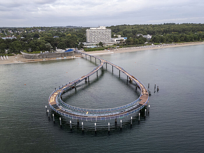 Seebrücke vor dem Maritim Seehotel Timmendorfer Strand mit ruhigem Wasser und blauem Himmel.