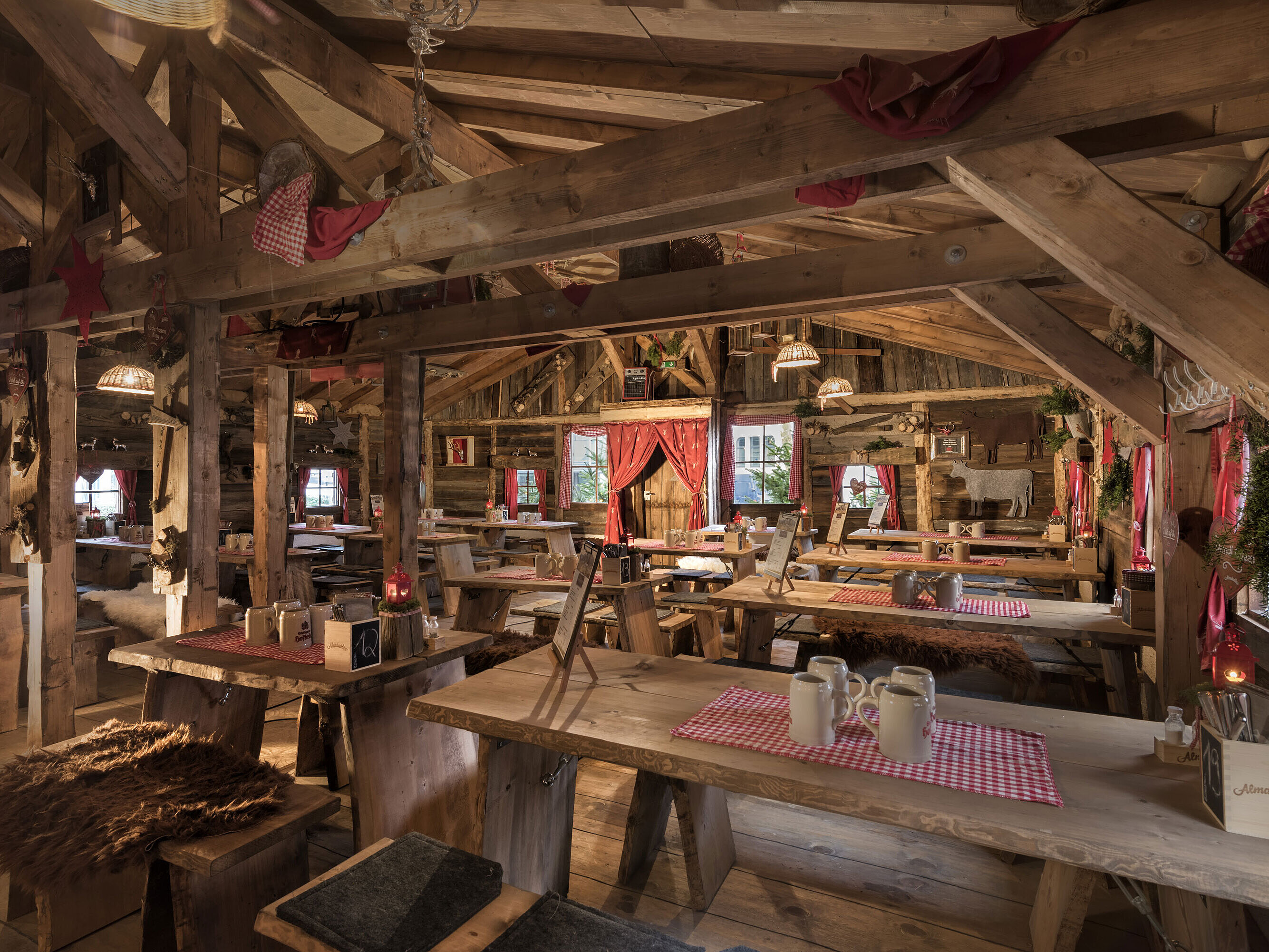 Almhütte Warmer Innenbereich mit Holztischen, roten Vorhängen und uriger Deko in der Maritim Alm Stuttgart