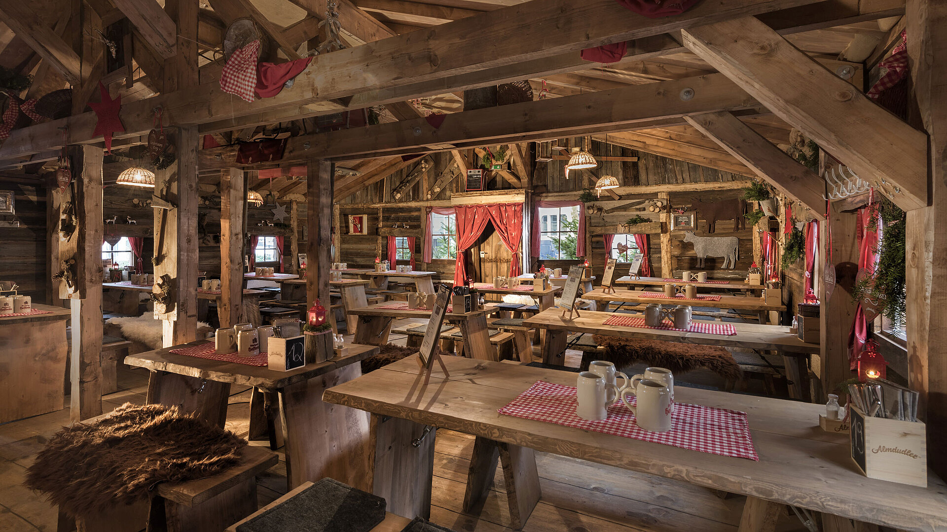 Almhütte Warmer Innenbereich mit Holztischen, roten Vorhängen und uriger Deko in der Maritim Alm Stuttgart